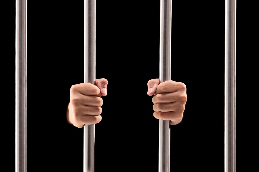 Male hands holding prison bars isolated on black background