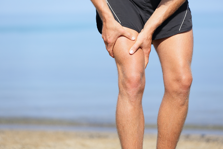 Muscle injury. Man with sprain thigh muscles. Athlete in sports shorts clutching his thigh muscles after pulling or straining them while jogging on the beach. Muscle injury. Man with sprain thigh muscles. Athlete in sports shorts clutching his thigh muscles after pulling or straining them while jogging on the beach.