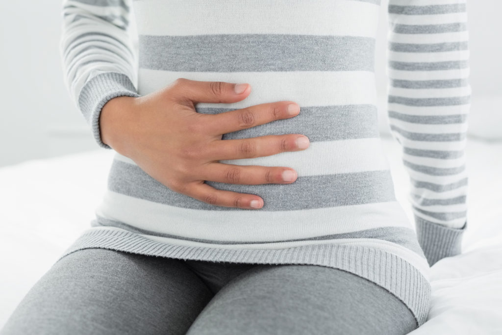Close-up mid section of a casual young woman with stomach pain sitting in bed at home Close-up mid section of a casual young woman with stomach pain sitting in bed at home